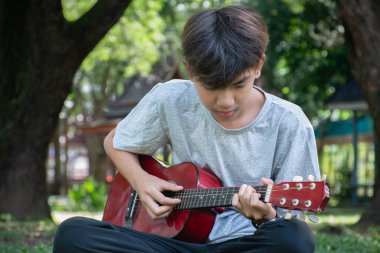 Evinin ön bahçesinde gitar çalan Asyalı sevimli çocuk mutlu, yumuşak odaklı, eğlence amaçlı aktivite konsepti ve dünyanın dört bir yanındaki çocukların boş zamanlarında hobileri..