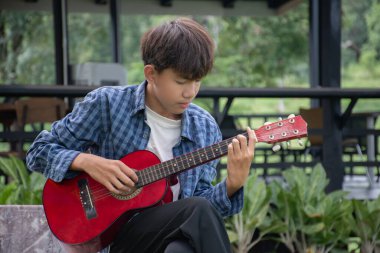 Evinin ön bahçesinde gitar çalan Asyalı sevimli çocuk mutlu, yumuşak odaklı, eğlence amaçlı aktivite konsepti ve dünyanın dört bir yanındaki çocukların boş zamanlarında hobileri..