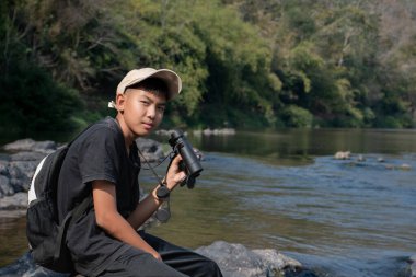 Asisn yakışıklı çocuk dürbünü tutuyor ve yerel ulusal parktaki kuş izleme etkinliğine katılıyor, yeni düzenlenmiş, dünyanın dört bir yanındaki gençlerin doğa ve çevre çalışmaları konsepti..