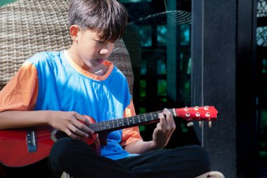 Asyalı yakışıklı çocuk evde akustik gitar, eğlence aktivitesi, hobi, boş zaman ve çocuk konsepti çalan popüler enstrümanlar çalıyor..