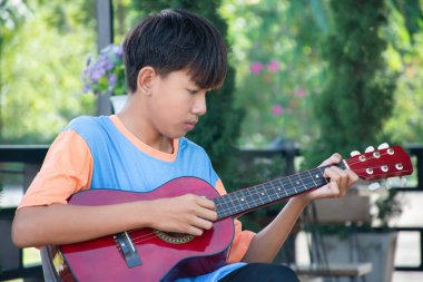 Asyalı tatlı çocuk evinin önünde oturup akustik gitar çalıyor, eğlence amaçlı aktiviteler, serbest zaman aktiviteleri ve dünya çapında erkeklerin hobileri..