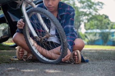 Bisikletin ön tekerleği düz ve kırık, arkasında Asyalı çocuk, yumuşak ve seçici tekerlek odaklı..