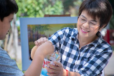  Asyalı okul çocuğu ve bayan sanat öğretmeni, sabah geç saatlerde okul parkında suluboya, posterboya ve resim, yeni düzenleme, açık hava öğrenimi konsepti ve yaz etkinliği hakkında bilgi topluyorlar..