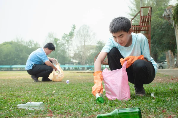 Asian boys are community volunteers collecting plastic drinking bottles and glass alcohol bottles in the community yard, concept for environmental protection of children, new edited.