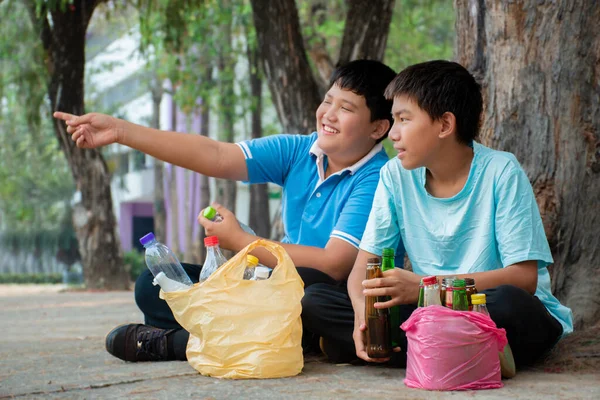 Asian boys are community volunteers collecting plastic drinking bottles and glass alcohol bottles in the community yard, concept for environmental protection of children, new edited.