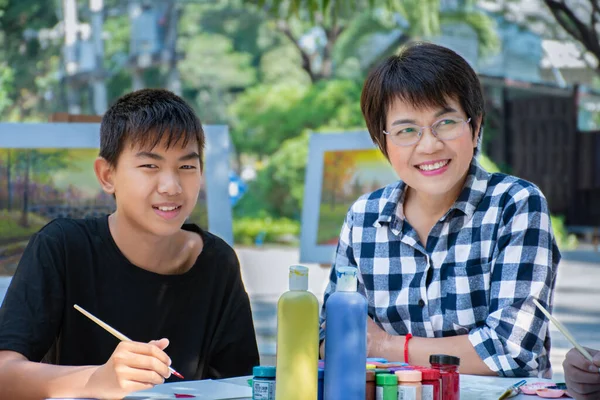 asian schoolboy  and their female art teacher are learing watercolor, postercolor and painting in schoolpark in late morning, new edited, concept for outdoor learning and summer activity.