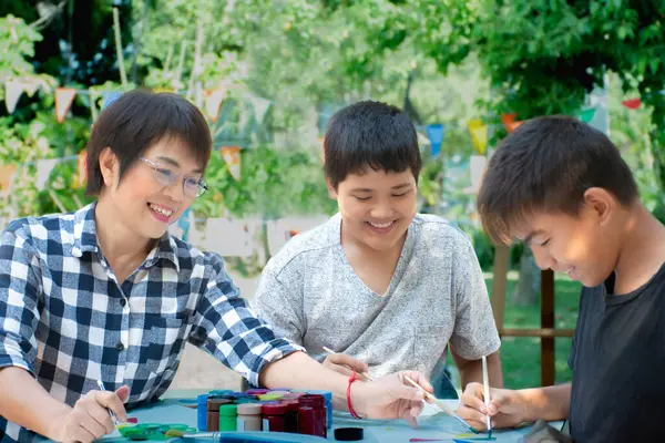 Group of asian schoolboys and their female art teacher are learing watercolor, postercolor and painting in schoolpark in late morning, new edited, concept for outdoor learning and summer activity.