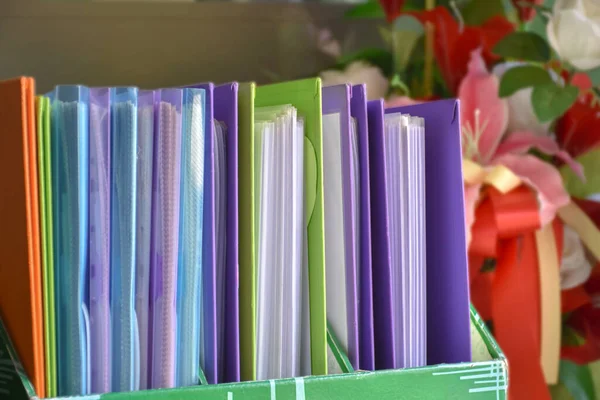 Back view of various plastic file folders for storing important documents in a file box for neatness and easy finding places near transparent glass window, blurred edited background.