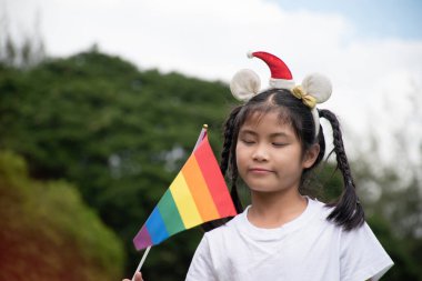 Asyalı tatlı kız, halk parkında gökkuşağı bayrakları tutuyor. Yumuşak ve seçici bir odak noktası. Dünyanın dört bir yanındaki insanları cinsiyet çeşitliliğine saygı duymaya ve LGBT etkinliklerini gurur ayında kutlamaya çağıran bir kavram..