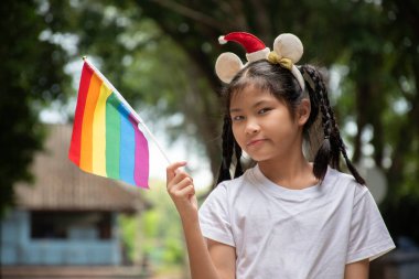 Asyalı tatlı kız, halk parkında gökkuşağı bayrakları tutuyor. Yumuşak ve seçici bir odak noktası. Dünyanın dört bir yanındaki insanları cinsiyet çeşitliliğine saygı duymaya ve LGBT etkinliklerini gurur ayında kutlamaya çağıran bir kavram..