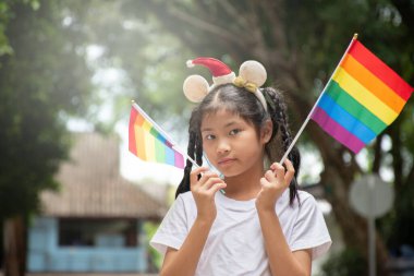Asyalı tatlı kız, halk parkında gökkuşağı bayrakları tutuyor. Yumuşak ve seçici bir odak noktası. Dünyanın dört bir yanındaki insanları cinsiyet çeşitliliğine saygı duymaya ve LGBT etkinliklerini gurur ayında kutlamaya çağıran bir kavram..