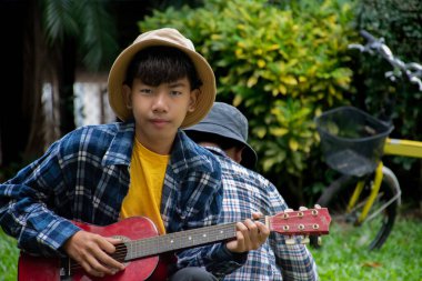 Asyalı çocuk okul parkında arkadaşıyla birlikte mutlu, yumuşak ve seçici bir şekilde akustik gitar çalıyor. Dünya çapında popüler enstrümanları olan çocukların mutluluğu konsepti..