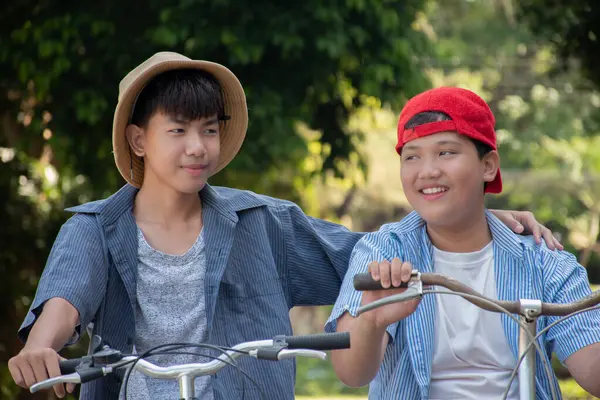Asian cute boy riding bicycle in the park with his friend and stopping to talk together before continued riding, soft and selective focus.