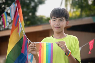 Asyalı oğlanlar gökkuşağı bayrağı, LGBT sembolü tutarlar, evlerinin önündeki çimenlikte otururlar. Evlerinin önündeki ağaçlarda asılı gökkuşağı teli bayrakları ile süslenmişlerdir..