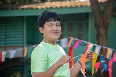 Asyalı oğlanlar gökkuşağı bayrağı, LGBT sembolü tutarlar, evlerinin önündeki çimenlikte otururlar. Evlerinin önündeki ağaçlarda asılı gökkuşağı teli bayrakları ile süslenmişlerdir..