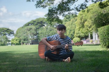 Asyalı sevimli çocuk sabahları evinin bahçesinde günışığıyla ukulele çalıyor..