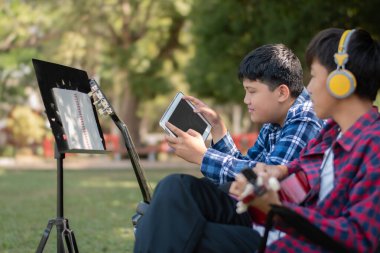 Asyalı sevimli çocuklar yaz etkinliklerini ön bahçelerinde akustik gitarlar çalarak ve göstererek yapıyor. Çocuk yaşam konseptinin serbest stili.