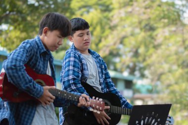 Asyalı sevimli çocuklar yaz etkinliklerini ön bahçelerinde akustik gitarlar çalarak ve göstererek yapıyor. Çocuk yaşam konseptinin serbest stili.