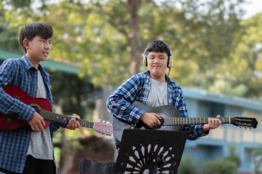 Asyalı sevimli çocuklar yaz etkinliklerini ön bahçelerinde akustik gitarlar çalarak ve göstererek yapıyor. Çocuk yaşam konseptinin serbest stili..