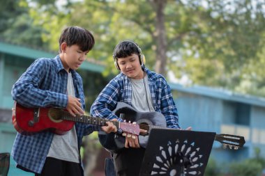 Asyalı sevimli çocuklar yaz etkinliklerini ön bahçelerinde akustik gitarlar çalarak ve göstererek yapıyor. Çocuk yaşam konseptinin serbest stili..