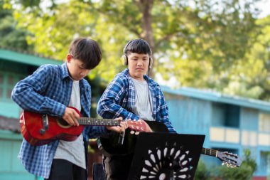 Asyalı sevimli çocuklar yaz etkinliklerini ön bahçelerinde akustik gitarlar çalarak ve göstererek yapıyor. Çocuk yaşam konseptinin serbest stili..