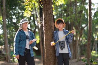 Asyalı bir okul çocuğu, ağaç gövdesi boyutunda bir mezura ile okul botanik bahçesi kütüphanesi için ağaçların bilgilerini kaydediyor..