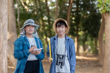 Asyalı bir okul çocuğu, ağaç gövdesi boyutunda bir mezura ile okul botanik bahçesi kütüphanesi için ağaçların bilgilerini kaydediyor..