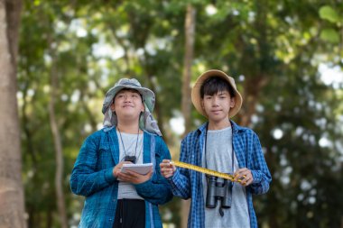 Asyalı bir okul çocuğu, ağaç gövdesi boyutunda bir mezura ile okul botanik bahçesi kütüphanesi için ağaçların bilgilerini kaydediyor..