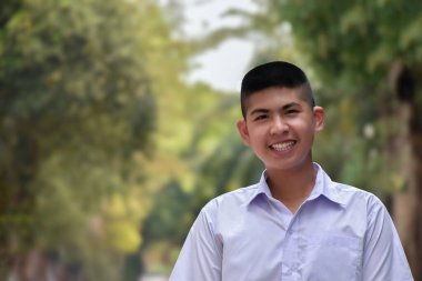 Kısa saçlı Asyalı yakışıklı okul çocuğu beyaz okul üniforması giyiyor ve büyük bir gülümseme takınıyor, yumuşak odaklanma, yüz ifadesi ve gülümseme..