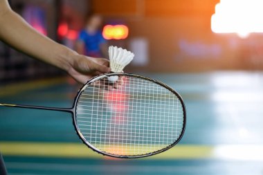Badminton oyuncusu, raketi ve beyaz kremalı mekikçiyi sahanın diğer tarafına götürmeden önce kalenin önünde tutuyor..