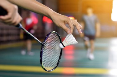 Badminton oyuncusu, raketi ve beyaz kremalı mekikçiyi sahanın diğer tarafına götürmeden önce kalenin önünde tutuyor..