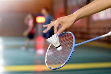 Badminton oyuncusu, raketi ve beyaz kremalı mekikçiyi sahanın diğer tarafına götürmeden önce kalenin önünde tutuyor..