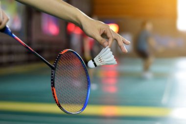 Badminton oyuncusu, raketi ve beyaz kremalı mekikçiyi sahanın diğer tarafına götürmeden önce kalenin önünde tutuyor..