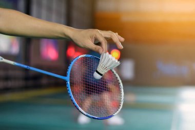 Badminton oyuncusu, raketi ve beyaz kremalı mekikçiyi sahanın diğer tarafına götürmeden önce kalenin önünde tutuyor..