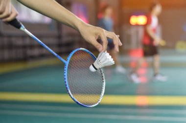 Badminton oyuncusu, raketi ve beyaz kremalı mekikçiyi sahanın diğer tarafına götürmeden önce kalenin önünde tutuyor..