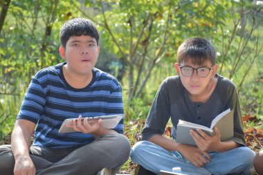 Bir grup Asyalı öğrenci parkta kitaplar ve dizüstü bilgisayarla çalışıyor..