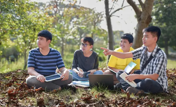 Group of asian students studying in the park with books and laptop computer.