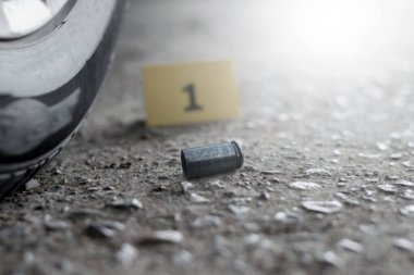 Araba tekerleğinin yanındaki bir numaralı sarı kağıdın önünde beton zeminde duran tabanca mermisi. Silah kullanarak soruşturma ve suç kavramı..