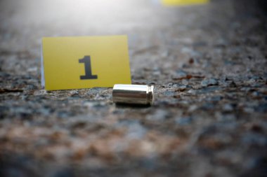 Araba tekerleğinin yanındaki bir numaralı sarı kağıdın önünde beton zeminde duran tabanca mermisi. Silah kullanarak soruşturma ve suç kavramı..