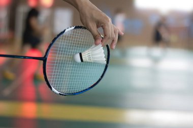 Badminton oyuncusu, raketi ve beyaz kremalı mekikçiyi sahanın diğer tarafına götürmeden önce kalenin önünde tutuyor.
