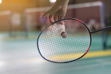 Badminton oyuncusu, raketi ve beyaz kremalı mekikçiyi sahanın diğer tarafına götürmeden önce kalenin önünde tutuyor.