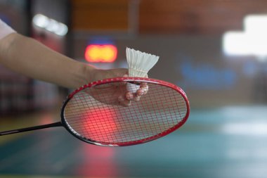 Badminton oyuncusu, raketi ve beyaz kremalı mekikçiyi sahanın diğer tarafına götürmeden önce kalenin önünde tutuyor.