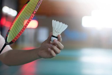 Badminton oyuncusu, raketi ve beyaz kremalı mekikçiyi sahanın diğer tarafına götürmeden önce kalenin önünde tutuyor.