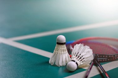 Krem beyazı badminton servis aracı ve kapalı badminton kortunda yeşil zeminde neon ışıklı raket, bulanık badminton kort arka planı, kopyalama alanı.