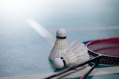 Krem beyazı badminton servis aracı ve kapalı badminton kortunda yeşil zeminde neon ışıklı raket, bulanık badminton kort arka planı, kopyalama alanı.