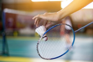 Badminton oyuncusu, raketi ve beyaz kremalı mekikçiyi sahanın diğer tarafına götürmeden önce kalenin önünde tutuyor..