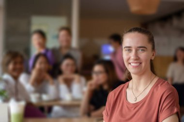 Young adult German woman sits in the middle of the cafe, soft focus, blurred people in cafe background. clipart