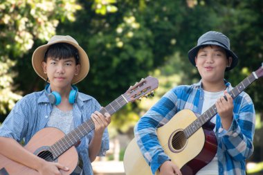 Asyalı çocuklar ellerinde akustik gitarlar, öğleden sonraları parklarında uzun bir yol yürüyorlar ve yaz tatili boyunca birlikte çalıyorlar, çocukların eğlence amaçlı aktiviteleri....