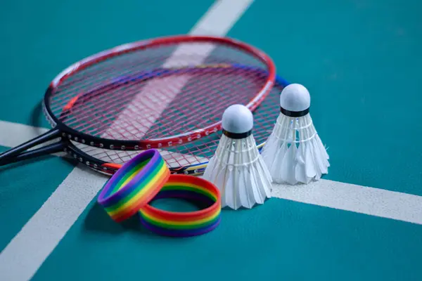 stock image Rainbow wristbands, used cream white badminton shuttlecock and racket placed on floor in indoor badminton court, copy space, soft and selective focus on shuttlecocks.