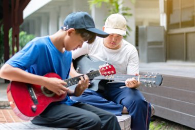 Asyalı sevimli çocuklar ellerinde akustik gitarlarla parkın terasındaki arkadaşıyla oynuyorlar. Popüler enstrüman konseptiyle çocuk eğlencesi yapıyorlar..